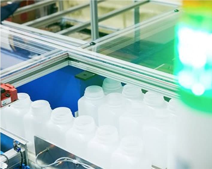 White plastic bottles moving through an automated production line enclosed in a protective frame, with a green signal light.