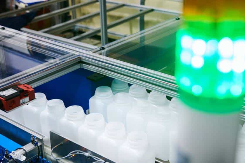 White plastic bottles moving through an automated production line enclosed in a protective frame, with a green signal light.