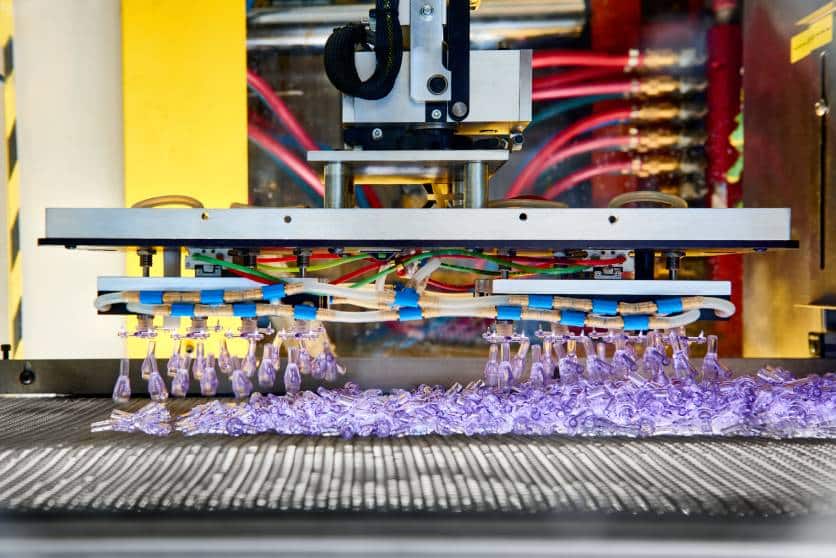 Automated robotic system handling freshly molded purple plastic components on a production line.