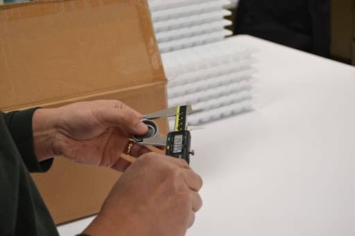 Person using a digital caliper to measure a plastic component for quality assurance.