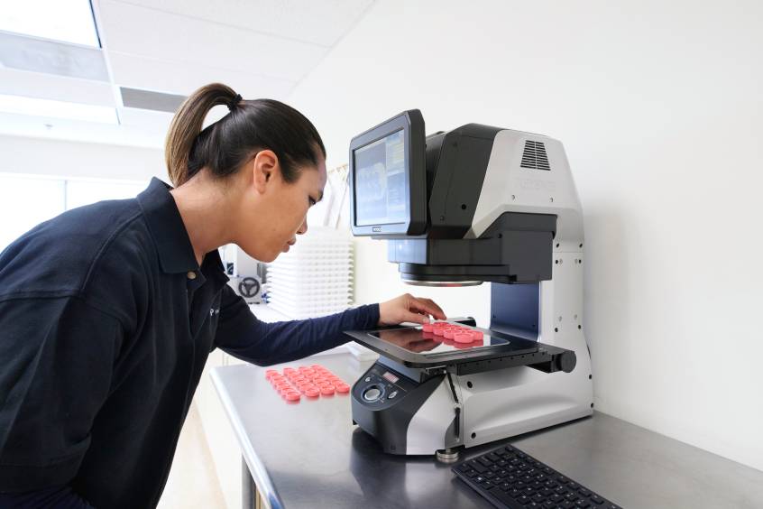 Technician inspecting molded plastic parts using a digital optical measurement system.