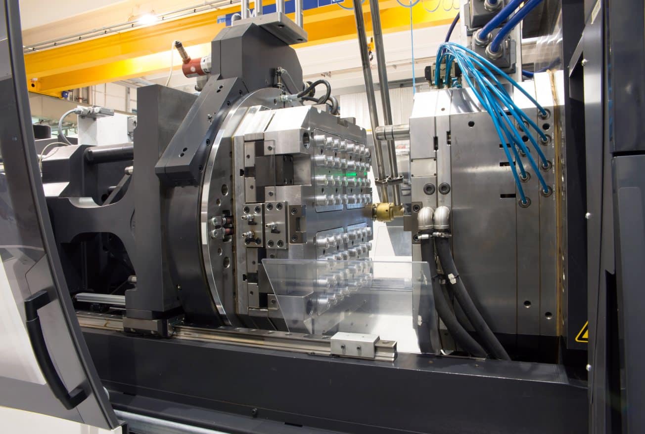 Injection molding machine with an open multi-cavity mold and visible hydraulic and cooling lines.