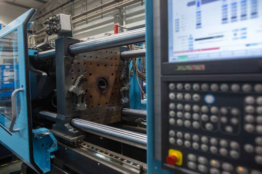 Close-up of an injection molding machine with control panel and exposed mold plate.