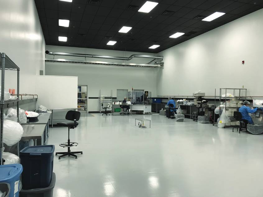 Spacious cleanroom facility with workstations and technicians in protective gear assembling medical products.