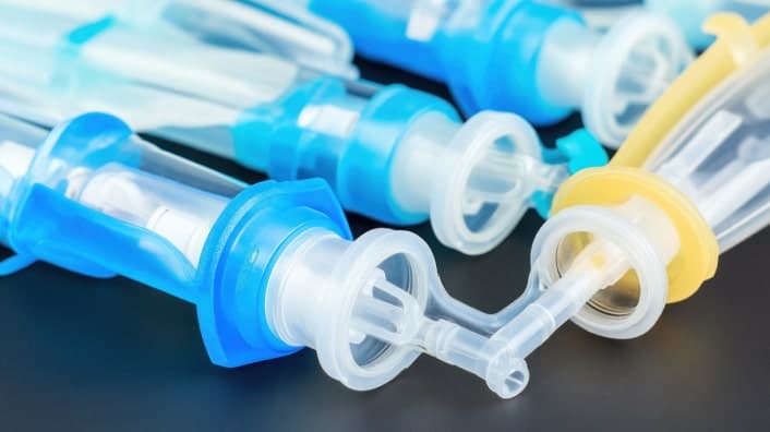 Close-up of sterile medical connectors and tubing components in blue and yellow, used for fluid transfer in healthcare applications.