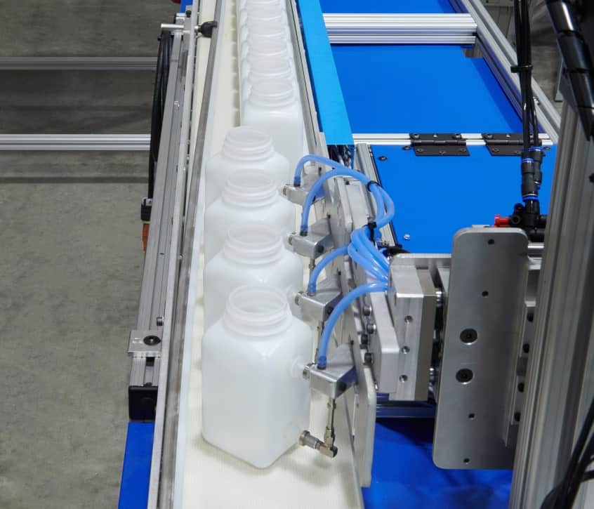 Close up of automated assembly line with white plastic bottles moving along a conveyor in a clean manufacturing facility.