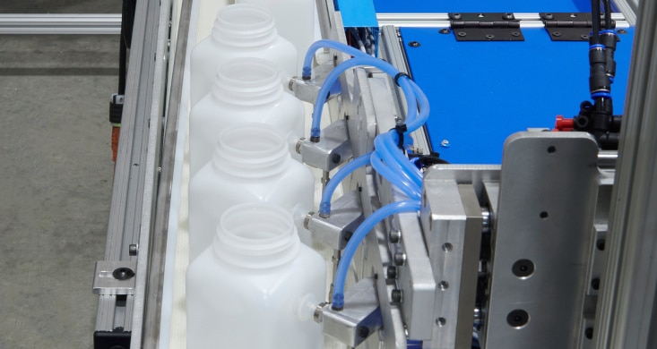 Close up of automated assembly line with white plastic bottles moving along a conveyor in a clean manufacturing facility.