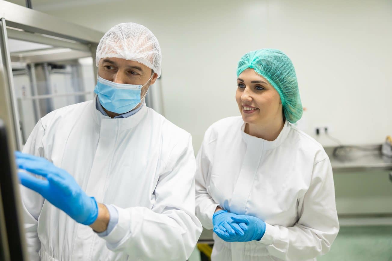 Two cleanroom technicians in protective gear while monitoring equipment in a sterile manufacturing environment.