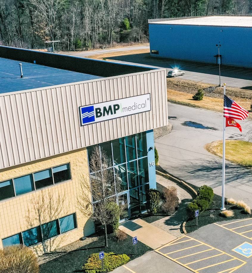 Exterior view of the BMP Medical facility with company signage, glass entryway, and American and state flags displayed out front.